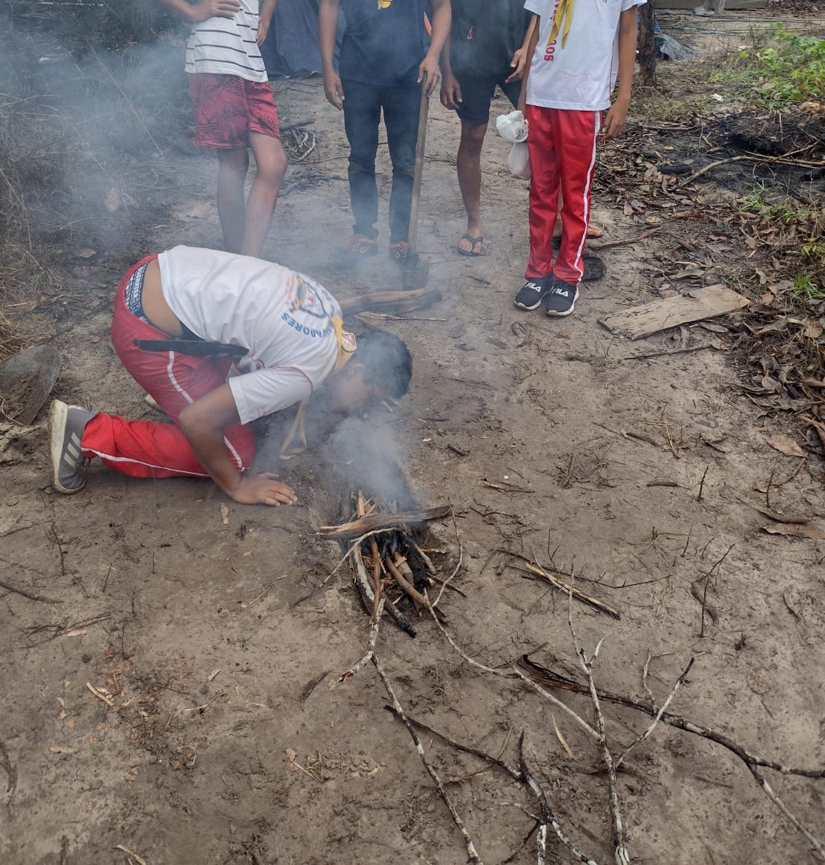 Desbravador soprando um pequeno fogo de gravetos no chão de terra