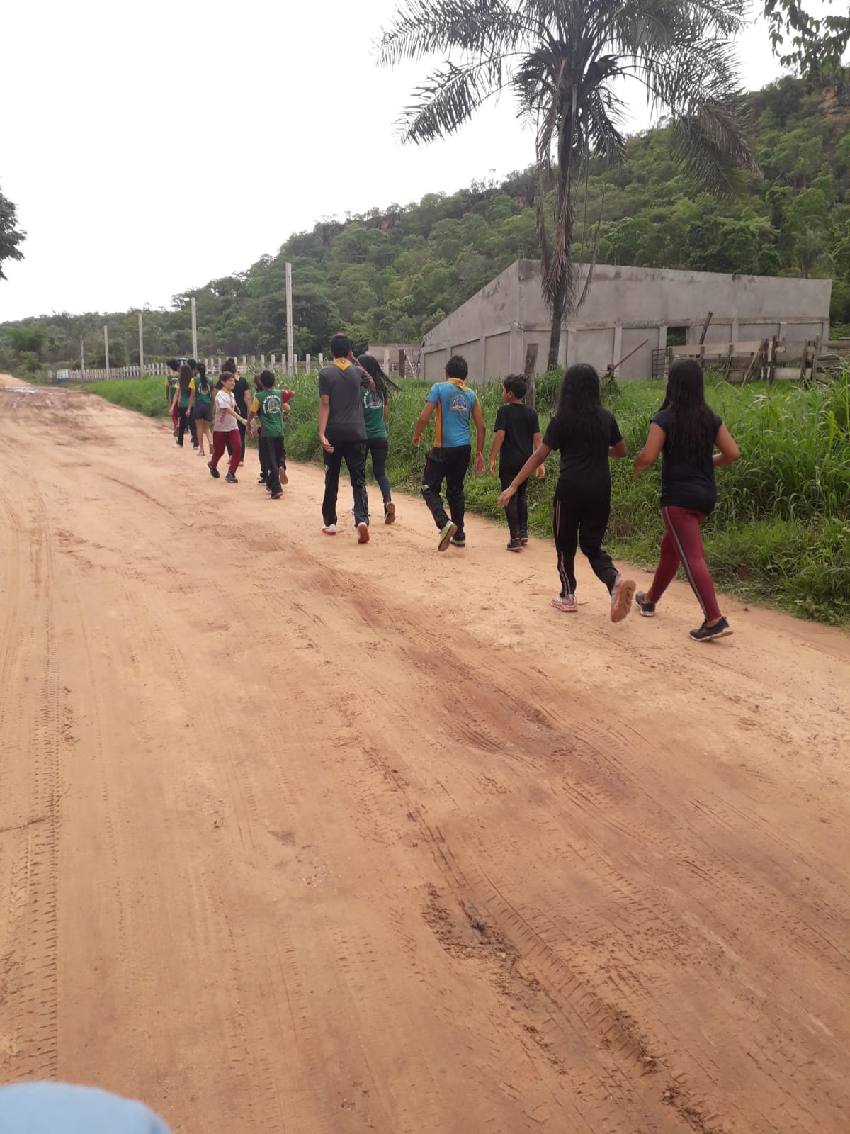 Desbravadores caminhando em fila por uma estrada de terra ao pé de um morro