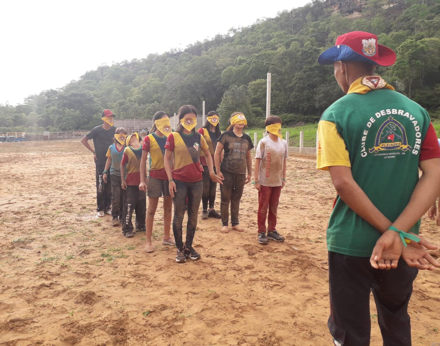 Fila de desbravadores com os olhos vendados pelo lenço amarelo, guiados por um líder de costas