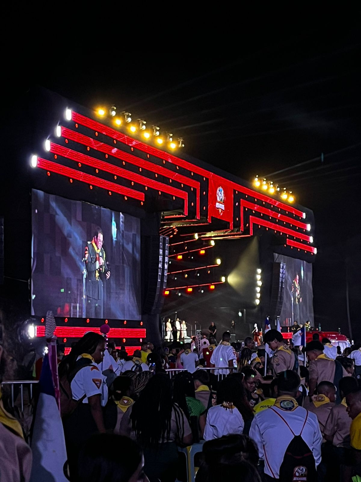 Palco com telões e luzes vermelhas e desbravadores de uniforme na plateia