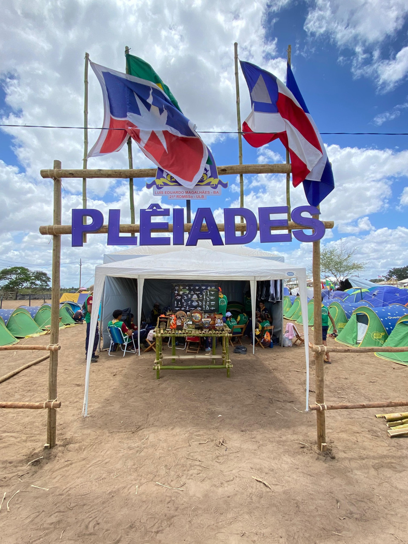 Portal de bambu com o nome Plêiades e as bandeiras na área de acampamento do clube