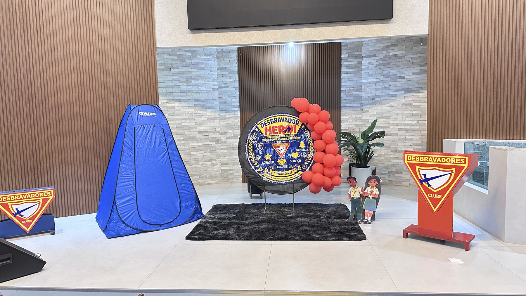 Palco decorado para a cerimônia de investidura, com emblema dos Desbravadores e balões vermelhos